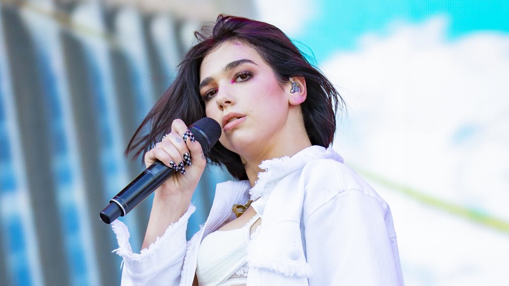 Dua Lipa singing at an outdoor concert, in a white outfit