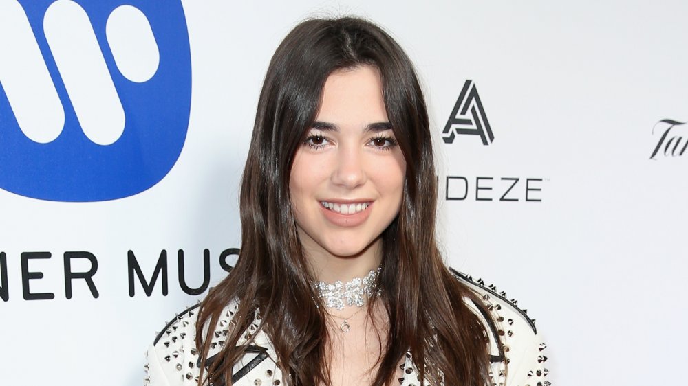 Dua Lipa smiling and wearing a bejeweled white outfit