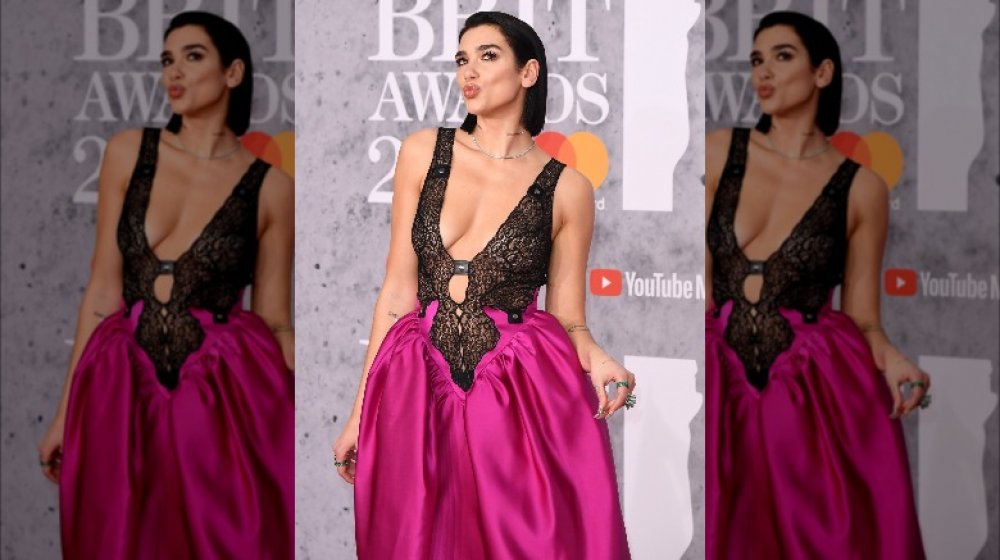 Dua Lipa making a kissy face while posing in a black-laced top and purple-skirted dress