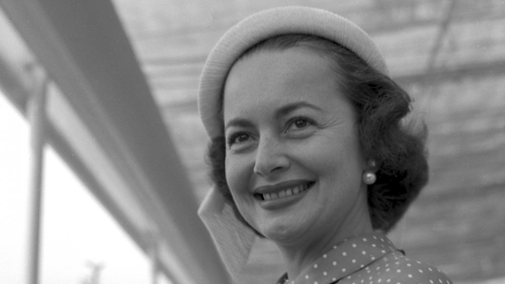 Photo en noir et blanc d'Olivia de Havilland portant un chapeau et des boucles d'oreilles en perles, souriant