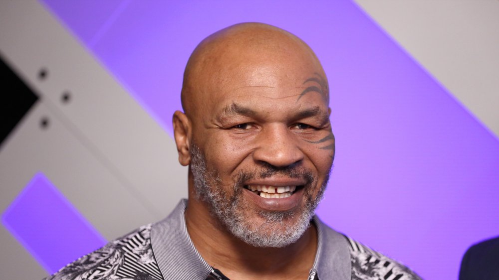 Mike Tyson souriant devant un mur violet