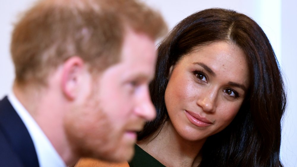 Le prince Harry parle avec Meghan Markle derrière lui