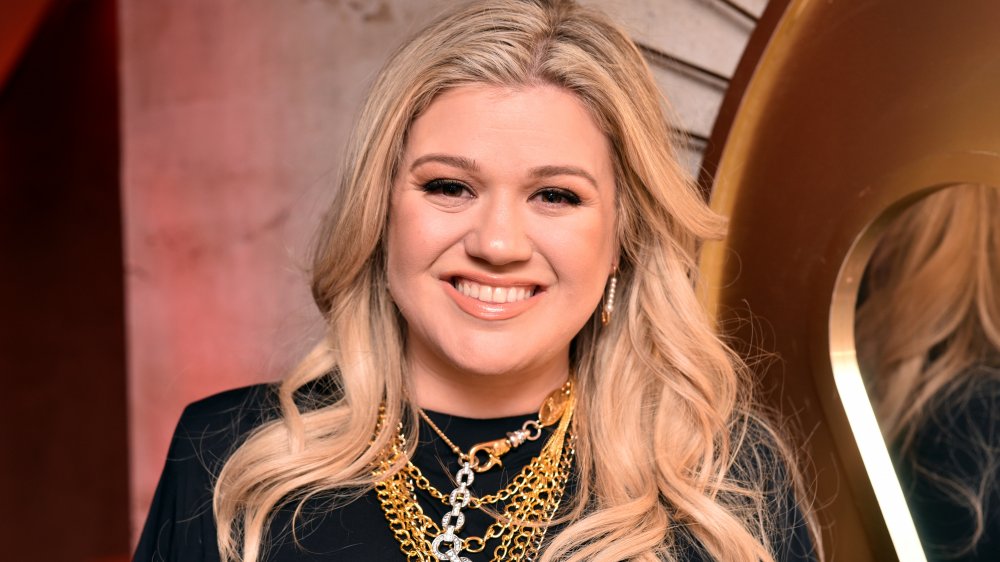 Kelly Clarkson dans une robe noire et des bijoux d’or, souriant