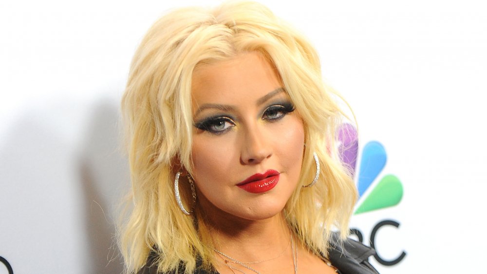 Christina Aguilera dans une veste en cuir noir et boucles d’oreilles cerceau d’argent, regardant l’appareil-photo avec une expression sérieuse