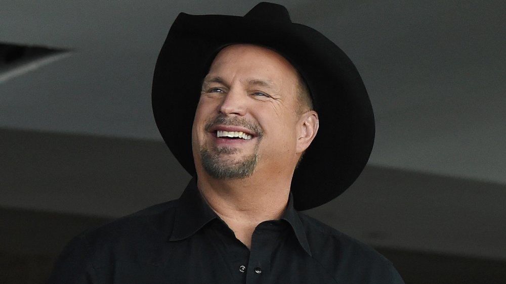 Garth Brooks dans une chemise boutonnée noire et un chapeau de cowboy, souriant tout en regardant vers le côté