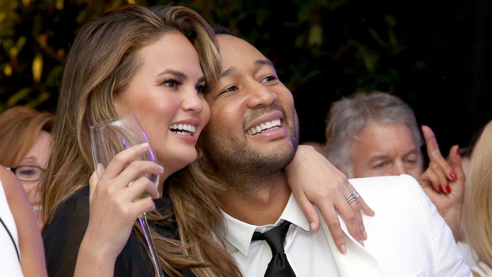 Chrissy Teigen tenant un verre de champagne, étreignant John Legend