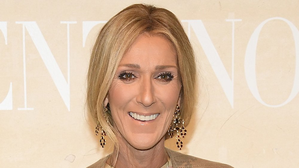 Céline Dion dans une tenue beige et boucles d’oreilles pendantes, souriant grande