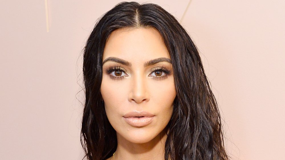 Kim Kardashian dans une robe blanche et le regard humide de cheveux, posant avec une expression étonnée