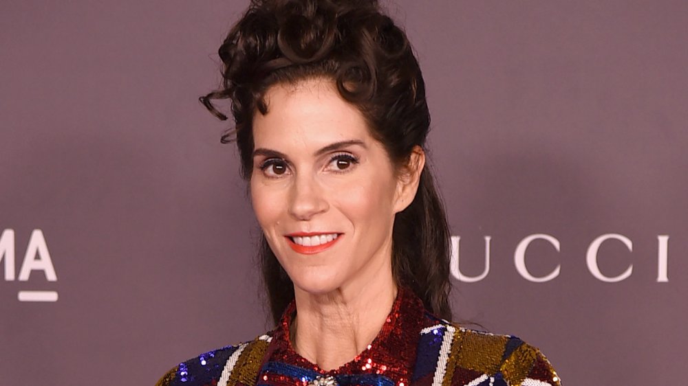 Jami Gertz dans une robe rouge, bleue et dorée scintillante, souriant et regardant sur le côté