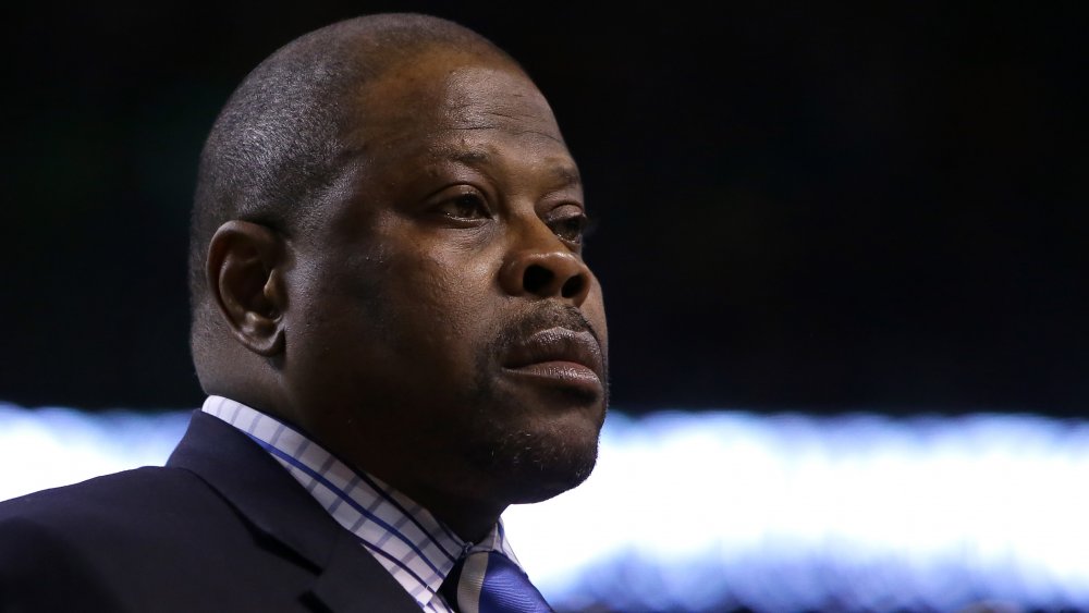 Patrick Ewing dans un blazer bleu et chemise à carreaux, regardant sur le côté avec une expression sérieuse