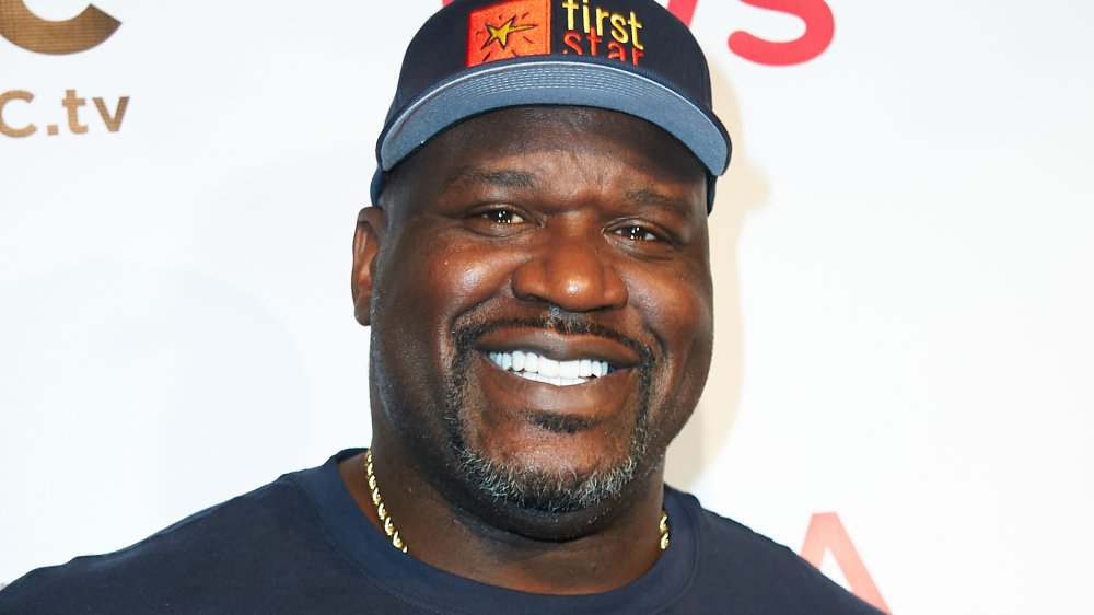 Shaquille O’Neal souriant dans un t-shirt et un chapeau bleus