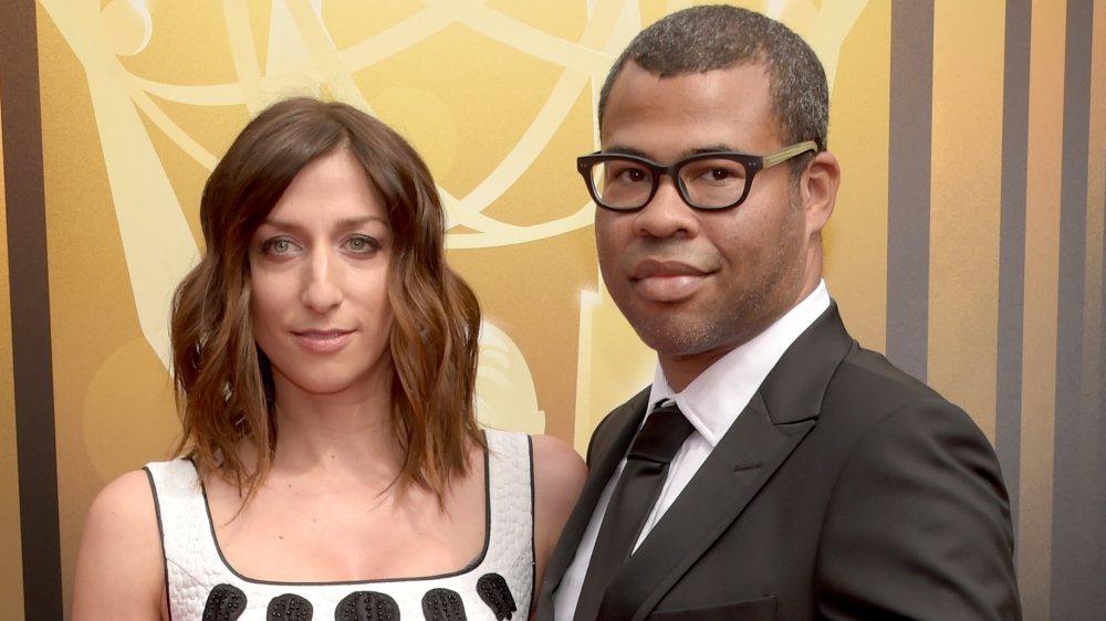 Chelsea Peretti dans une robe blanche et noire, Jordan Peele dans un costume noir et des lunettes