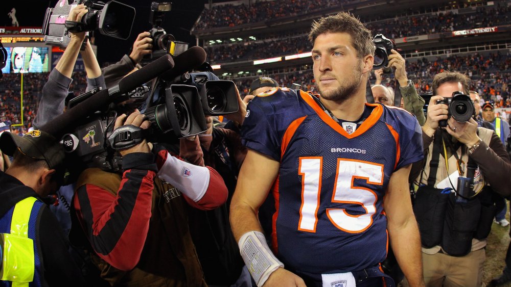 Tim Tebow dans un uniforme des Broncos de Denver, entouré de journalistes