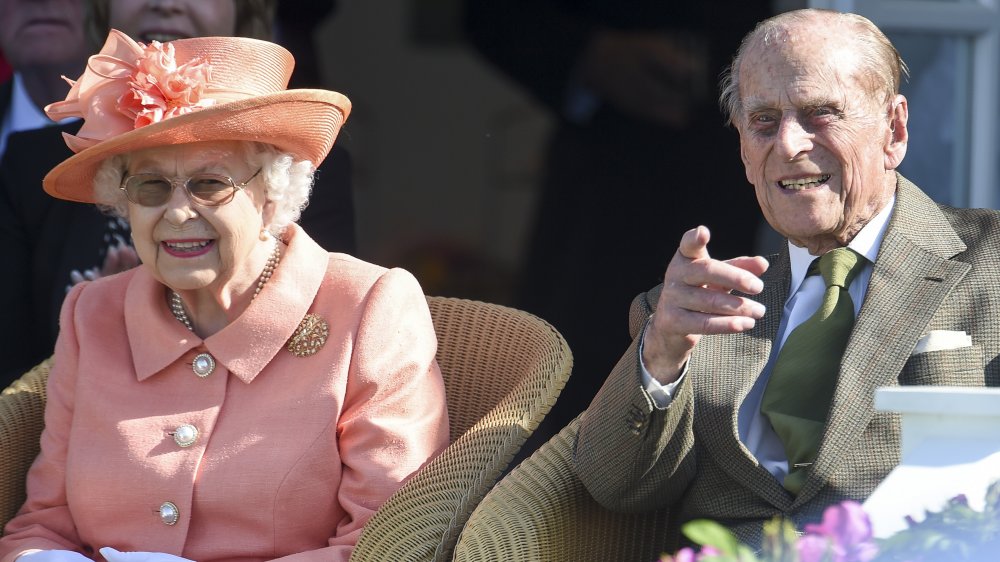 La reine dans un ensemble de couleur saumon et le prince Philip, pointant