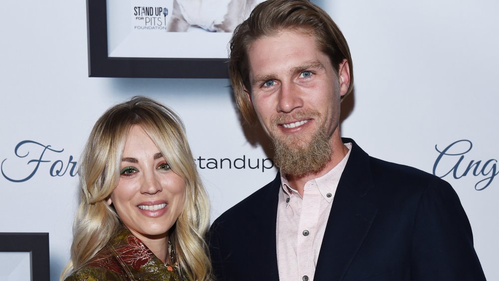 Kaley Cuoco et Karl Cook devant un mur promotionnel, souriant