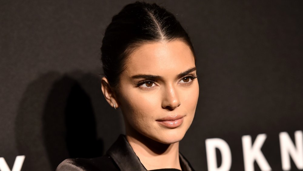 Kendall Jenner avec ses cheveux lissés en arrière devant le mur noir