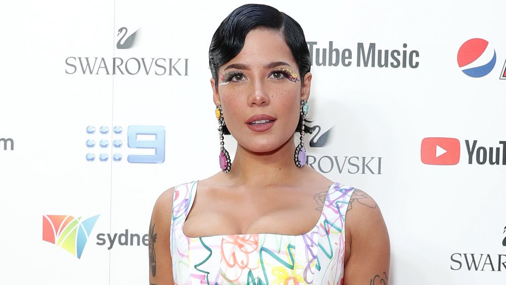 Halsey avec les cheveux noirs courts, maquillage coloré d’oeil, et boucles d’oreilles longues