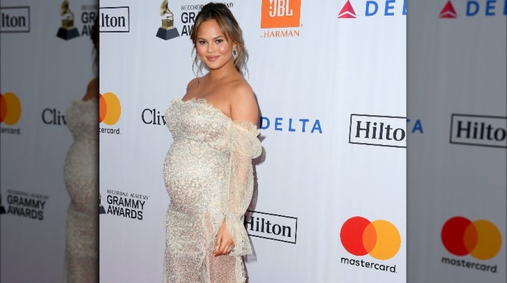 Chrissy Teigen posant de côté et souriante, montrant sa bosse de bébé