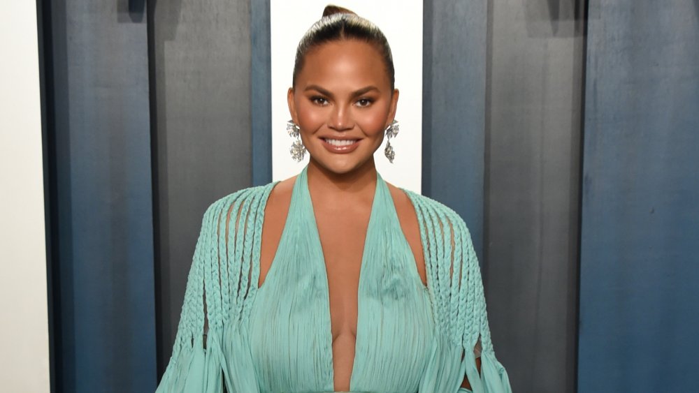 Chrissy Teigen sourit en posant dans une robe bleu clair à la Vanity Fair Oscar Party 2020