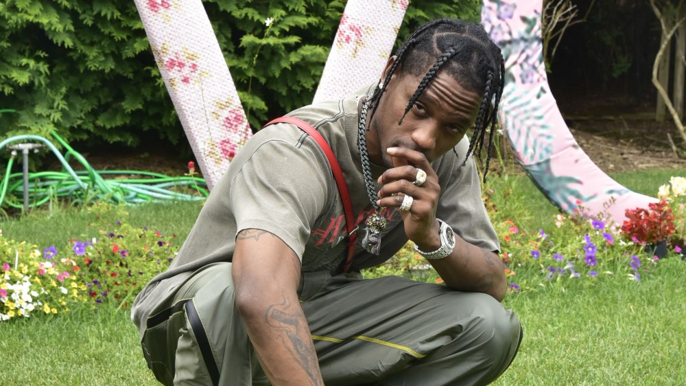 Travis Scott accroupi avec une main sur sa bouche