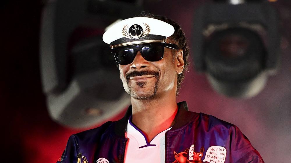 Snoop Dogg souriant sur scène portant des lunettes de soleil aviateur et une visière