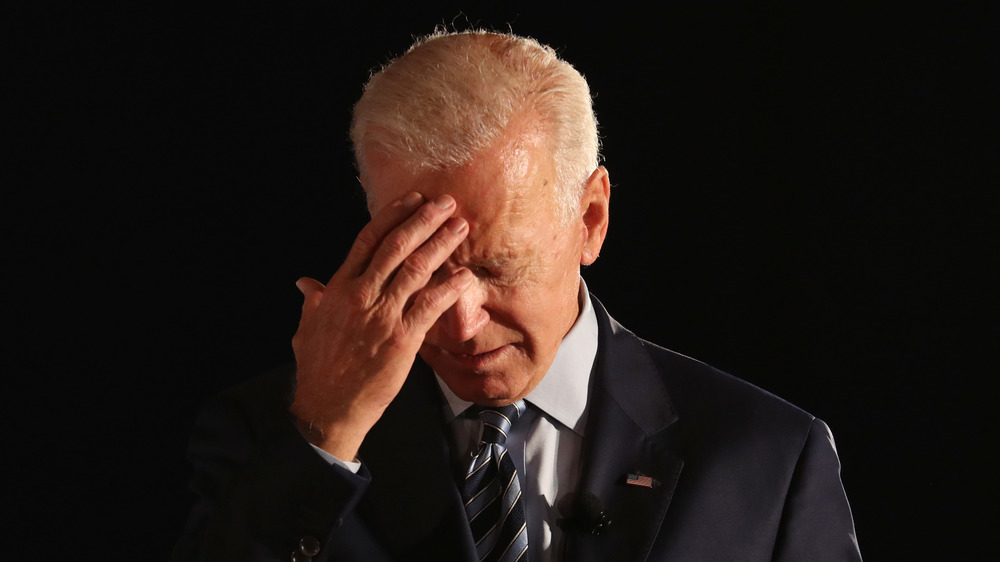 Joe Biden regardant vers le bas, touchant son front 