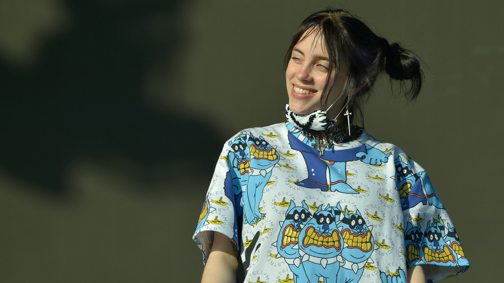 Billie Eilish souriant et portant un masque sous son menton