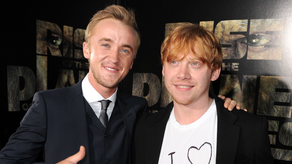 Tom Felton et Rupert Grint souriant tout en posant bras dessus bras dessous lors d'une première de film