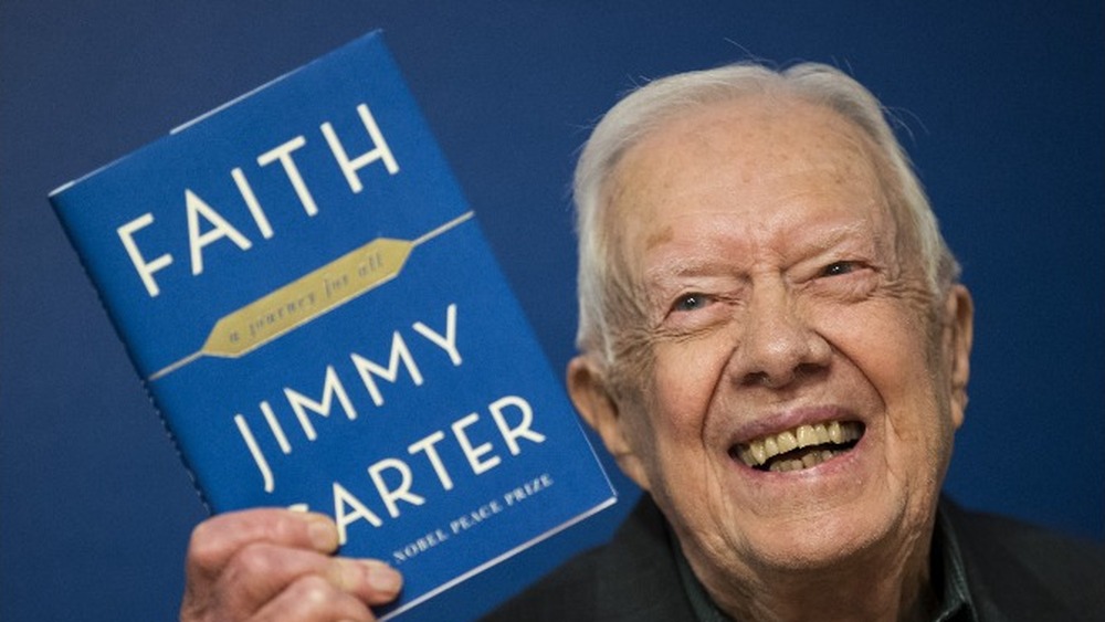 L'ancien président américain Jimmy Carter brandit un exemplaire de `` Faith: A Journey For All '' lors d'un événement de signature de livre en 2018