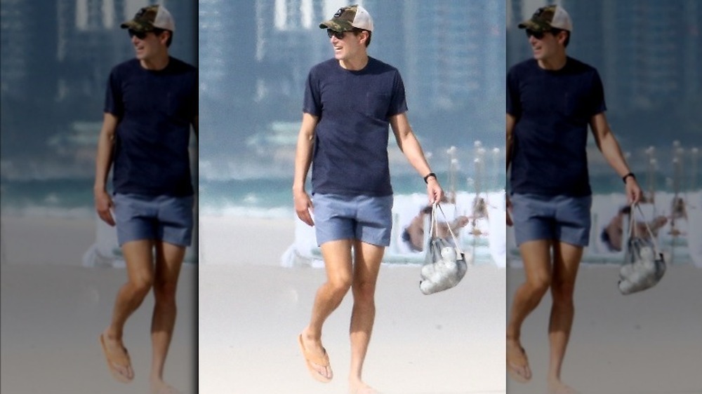 Jared Kushner sur la plage souriant, portant un maillot de bain et des sandales 