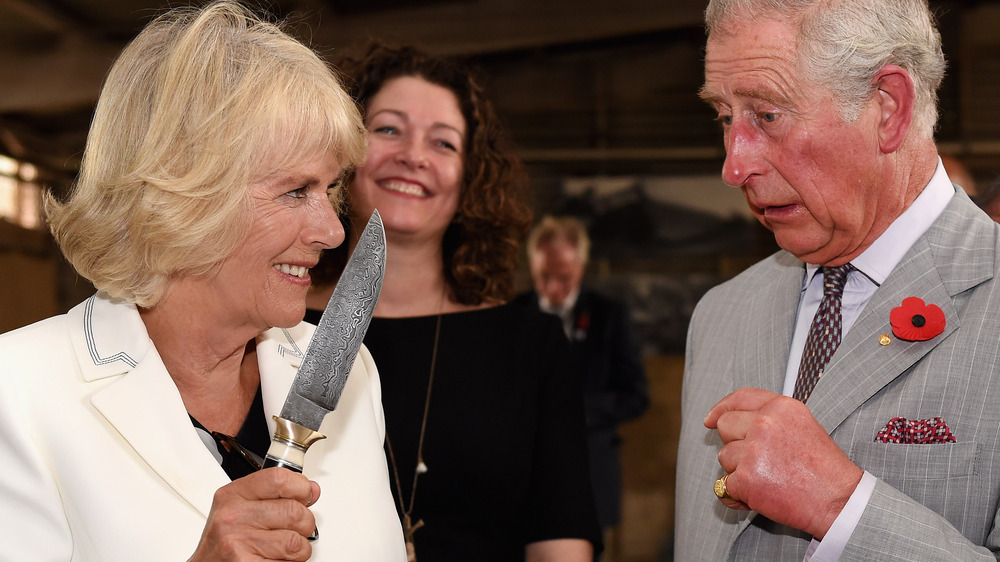 Camilla duchesse de Cornouailles brandissant un couteau en plaisantant sur le prince Charles