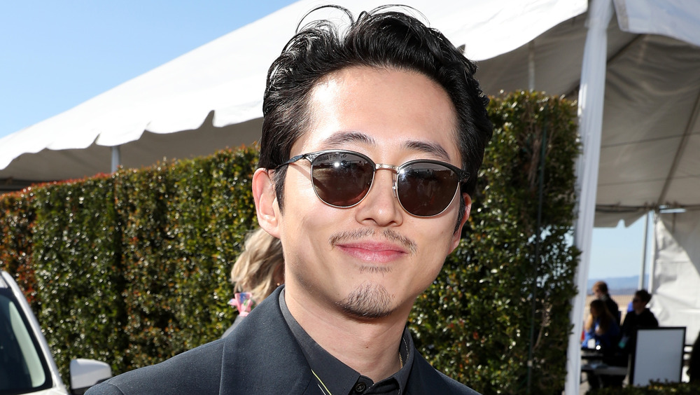 Steven Yeun souriant à lunettes de soleil