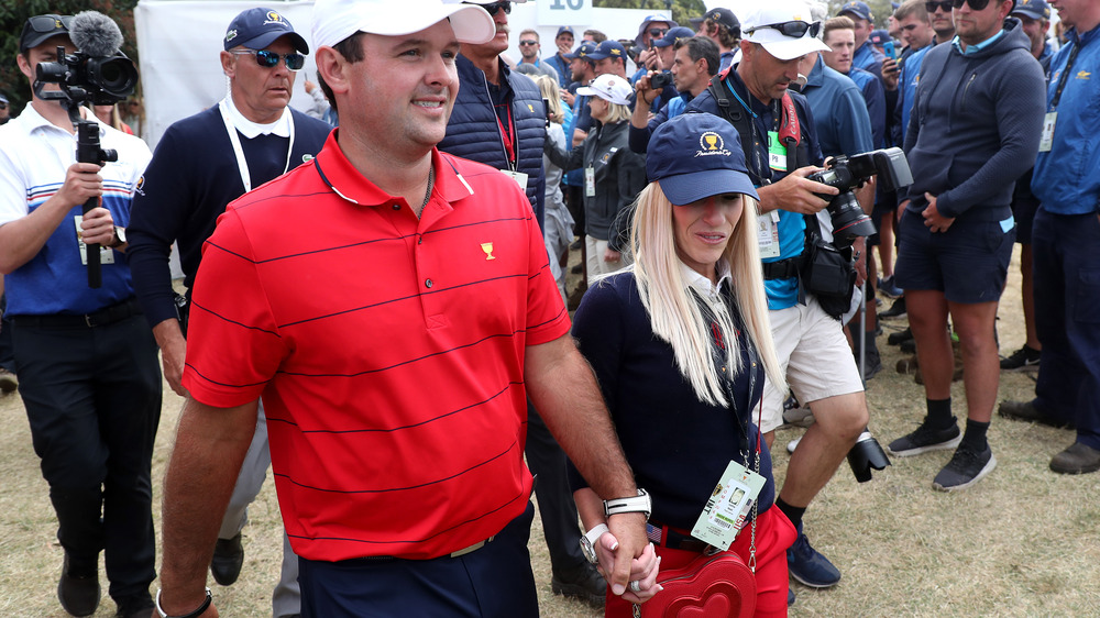 Patrick Reed et Justine Reed marchant main dans la main, tous deux coiffés de chapeaux, entourés de photographes et de fans 