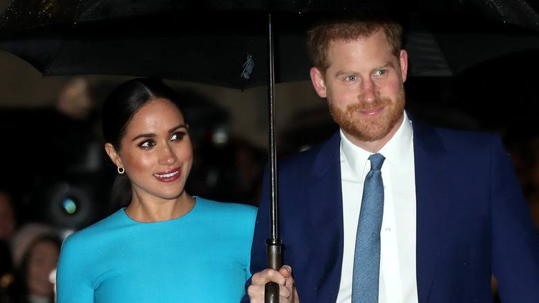 Meghan Markle et le prince Harry souriant sous un parapluie