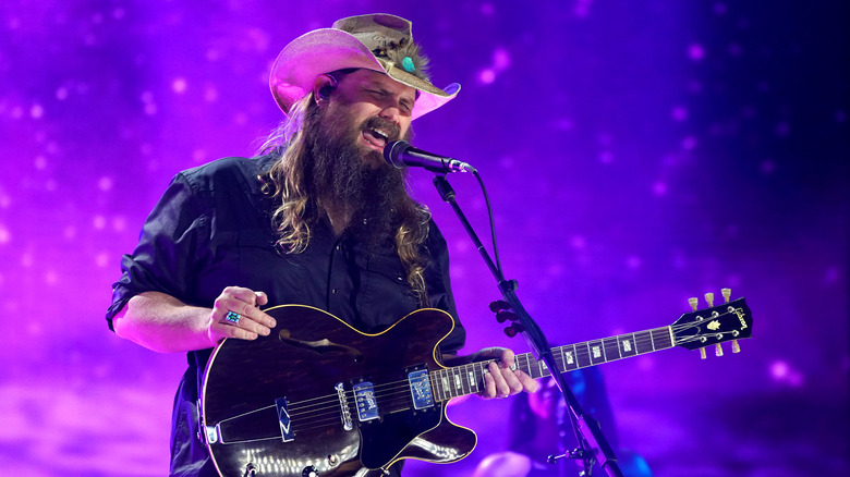 Chris Stapleton, portant un chapeau de cowboy, jouant de la guitare et chantant sur scène en 2021