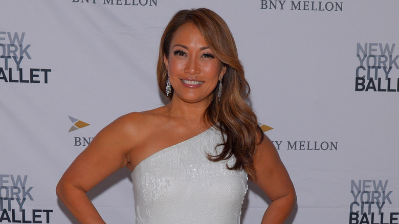 Carrie Ann Inaba avec un large sourire portant un haut blanc à une épaule