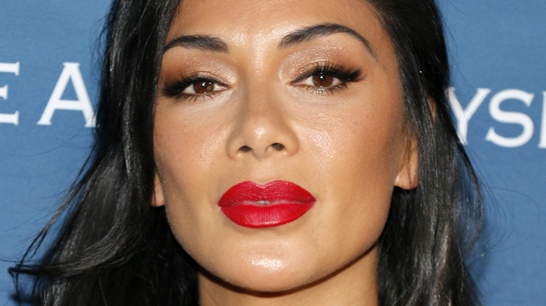 Nicole Scherzinger regardant la caméra avec une expression sérieuse et un rouge à lèvres rouge