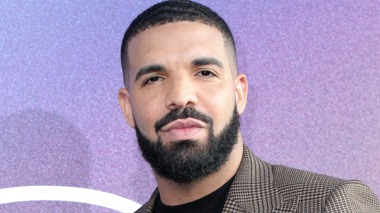 Drake regarde, vêtu d'un blazer à carreaux