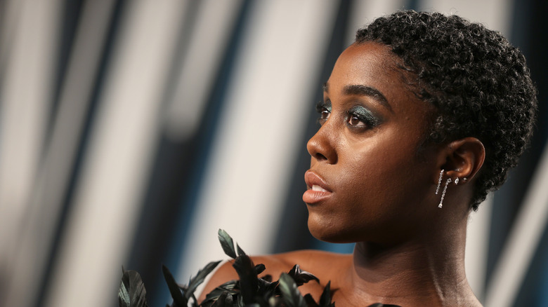 Lashana Lynch pose dans une robe noire à plumes.