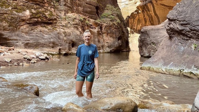 Gabby Petito souriant, pataugeant dans l'eau parmi les montagnes