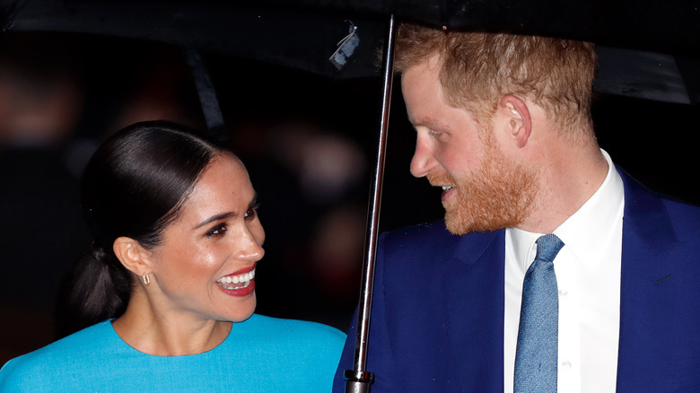 Meghan and Harry smiling at each other under an umbrella