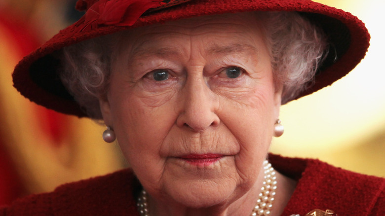 La reine Elizabeth II avec une expression sérieuse et un chapeau rouge