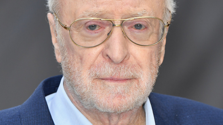 Michael Caine portant des lunettes sur le tapis rouge avec un léger sourire