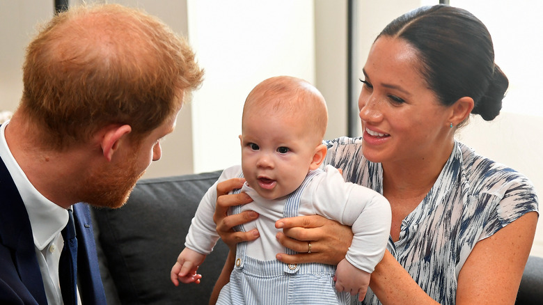 Le prince Harry assis avec Meghan Markle tenant Archie