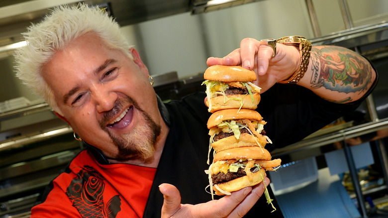 Guy Fieri tenant trois hamburgers empilés