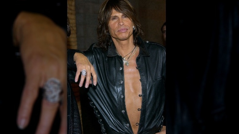 Steven Tyler à la recherche d'un tanneur dans une chemise en cuir ouverte et un rouge à lèvres rose