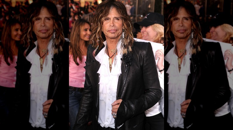 Steven Tyler posant dans un blazer en cuir et une chemise blanche à froufrous