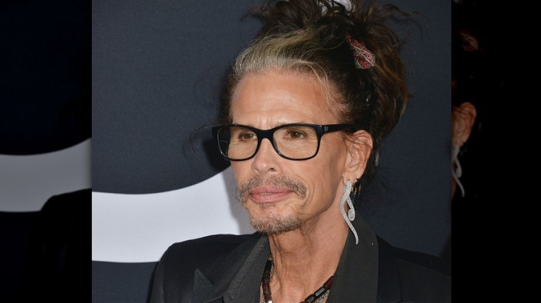 Steven Tyler portant des lunettes sur le tapis rouge dans un costume noir avec des cheveux en chignon