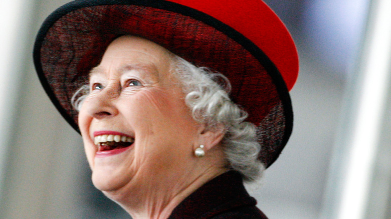 La reine Elizabeth rit avec un chapeau et une tenue rouges et noirs 