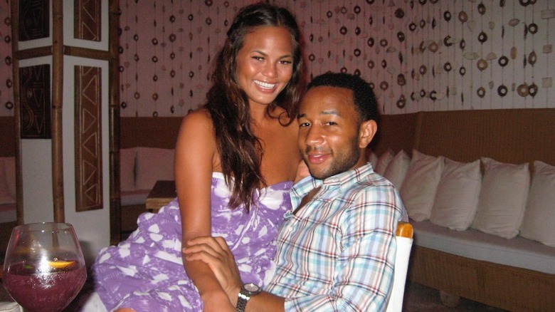 Chrissy Teigen assise sur les genoux de John Legend en souriant